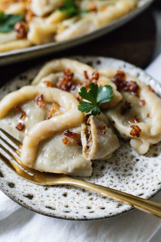 Close-up of delicious pierogi with fried onions, served on a speckled plate.
