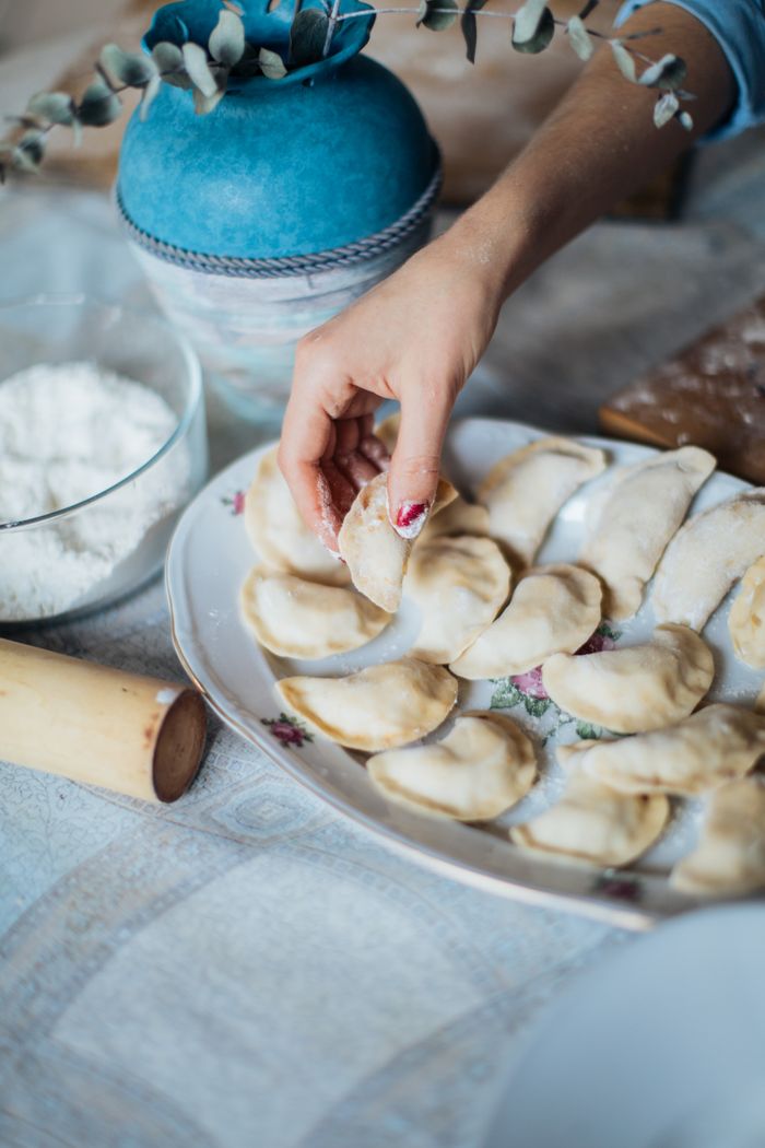 A close-up of a woman's hands making traditional pelmeni with dough and flour.