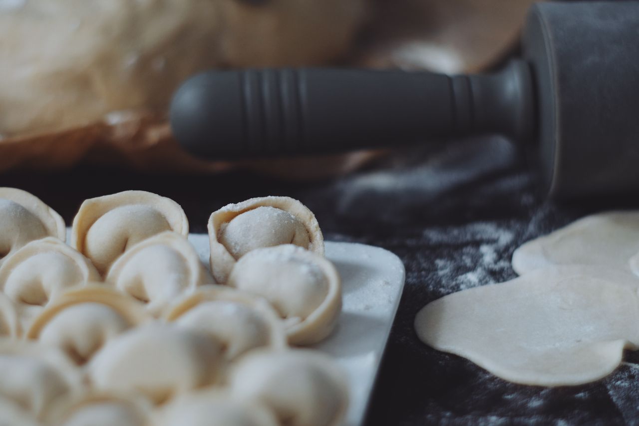 Close-up view of uncooked Russian pelmeni dumplings with dough on a dark surface, ready to cook.