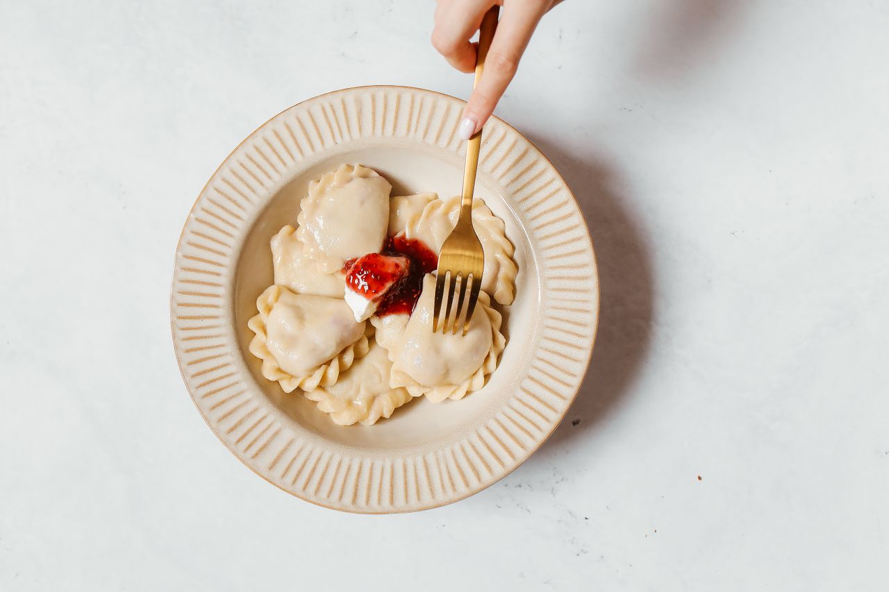 Aerial shot of a hand holding a fork over pierogi topped with strawberries.